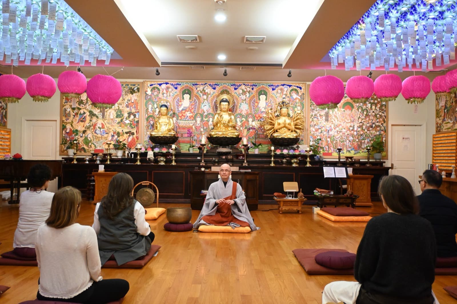 The sangha seated in meditation as Venerable SooSeong teaches beneath the temple's lotus lanterns.